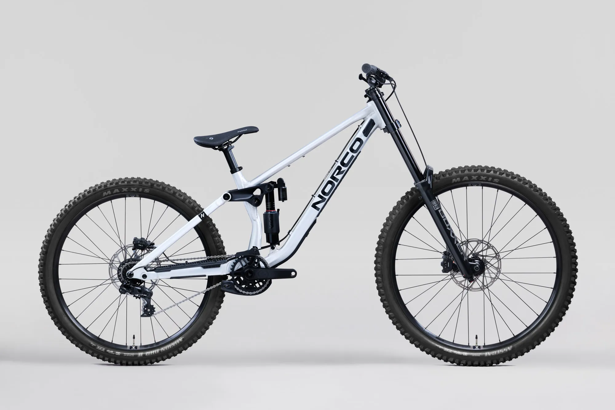 Norco Torrent DH A1 2027 aluminium brut, vue de profil, roue avant à droite : cadre argenté, transmission et plateau visibles côté chaîne, pneus Maxxis à gros crampons.